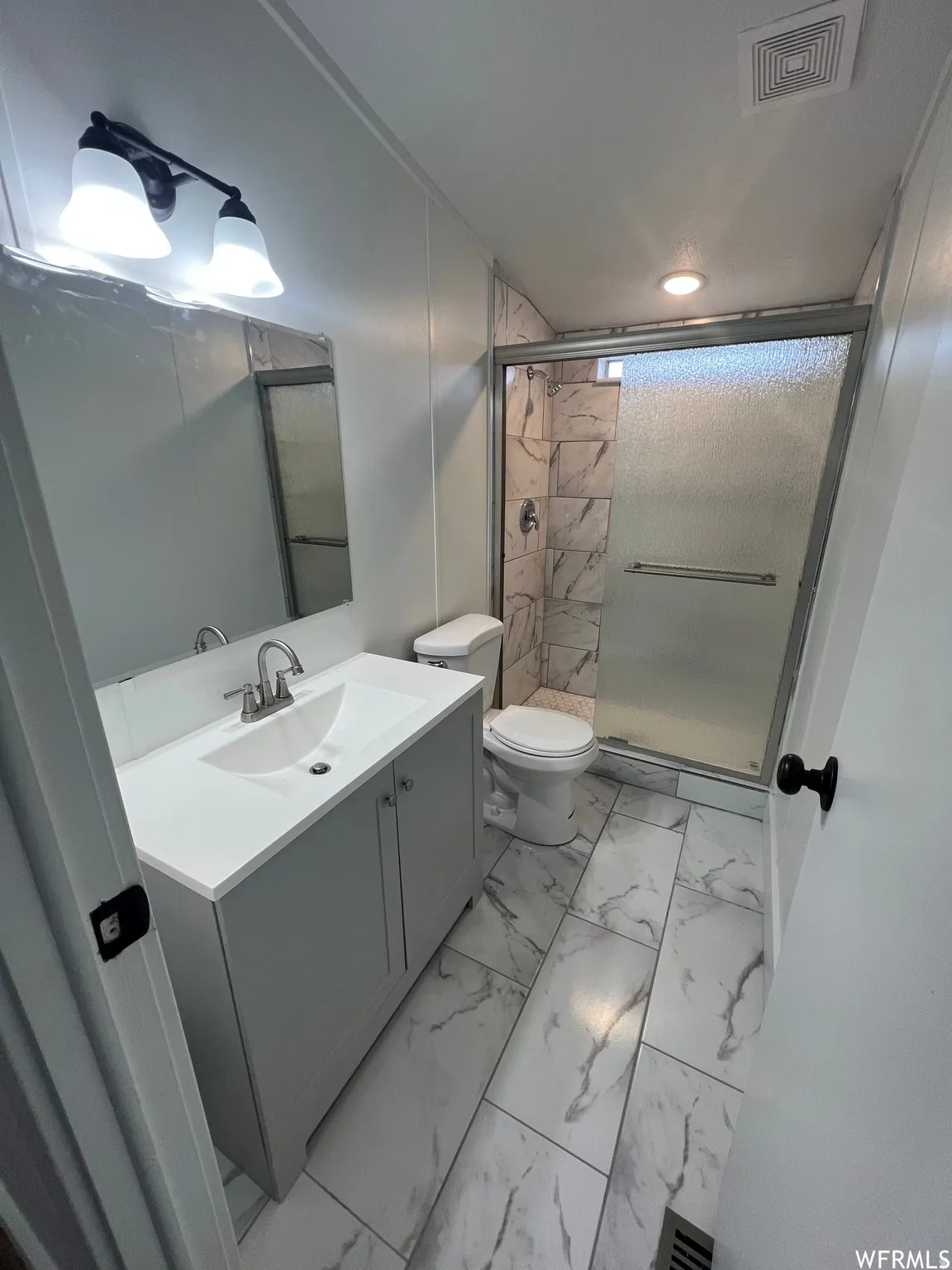 Full bathroom featuring vanity, light marble finish floors, and a stall shower