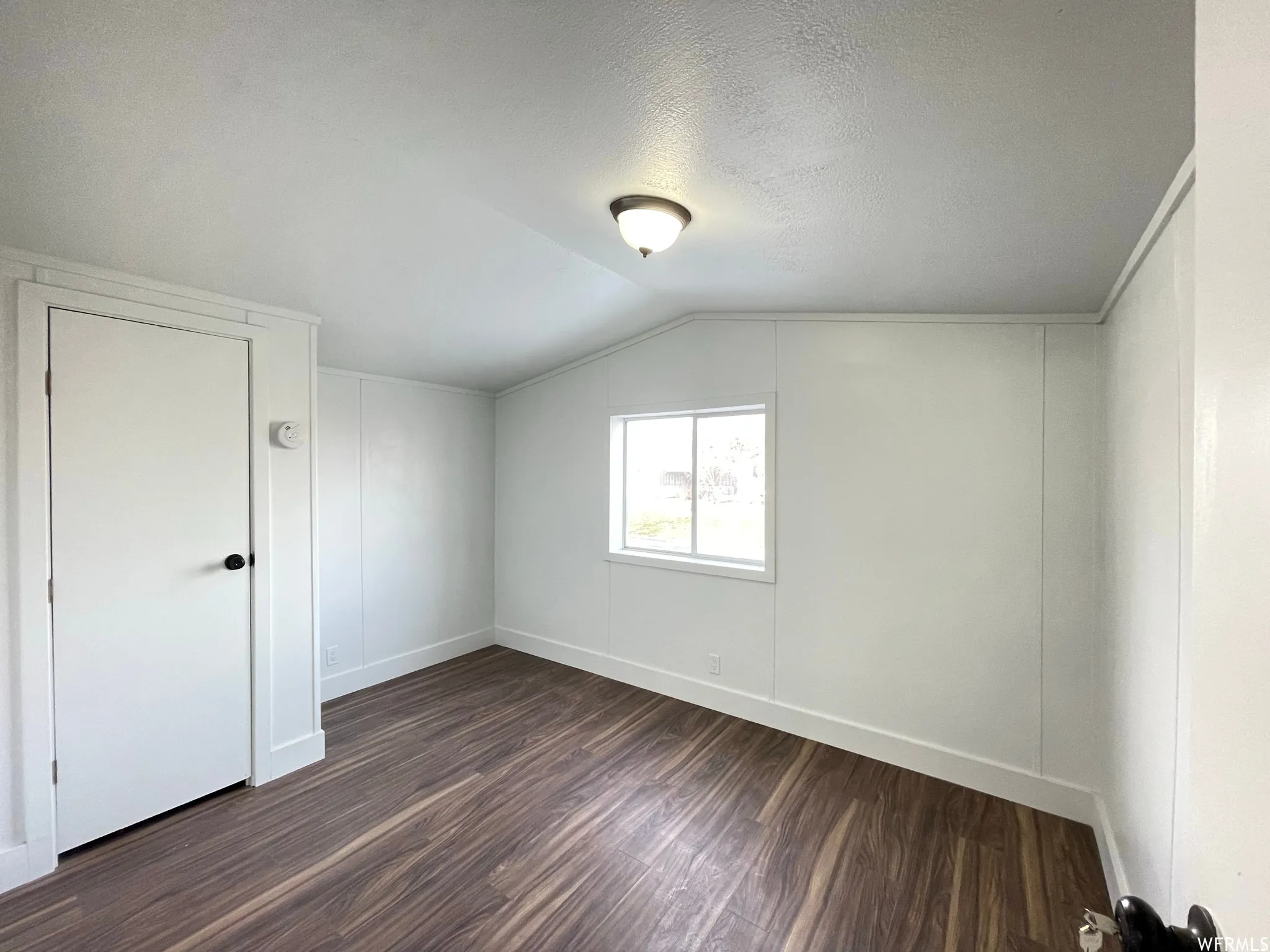 Additional living space with dark wood-type flooring, a textured ceiling, and vaulted ceiling