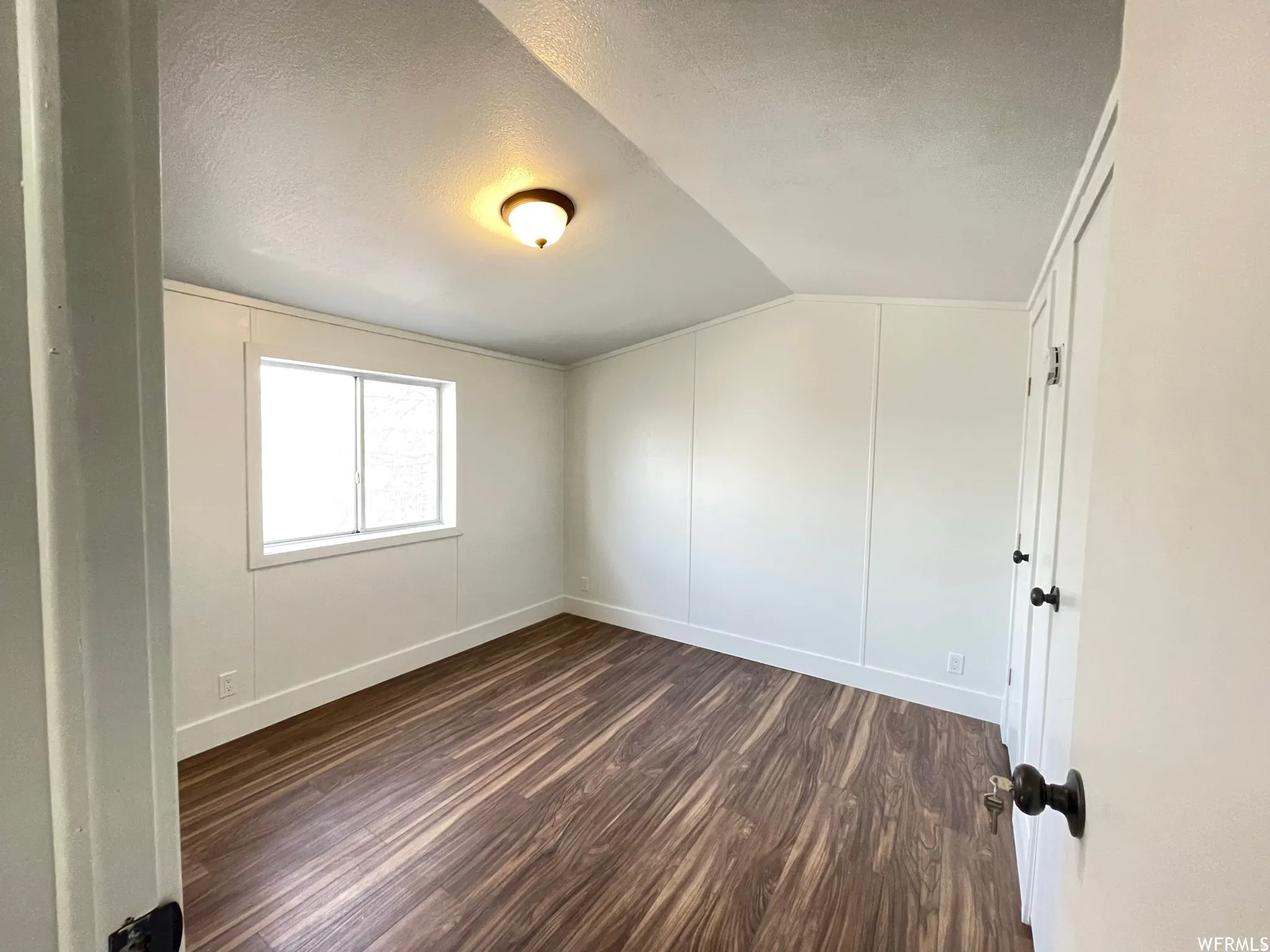 Empty room with dark wood-style floors, a textured ceiling, and vaulted ceiling