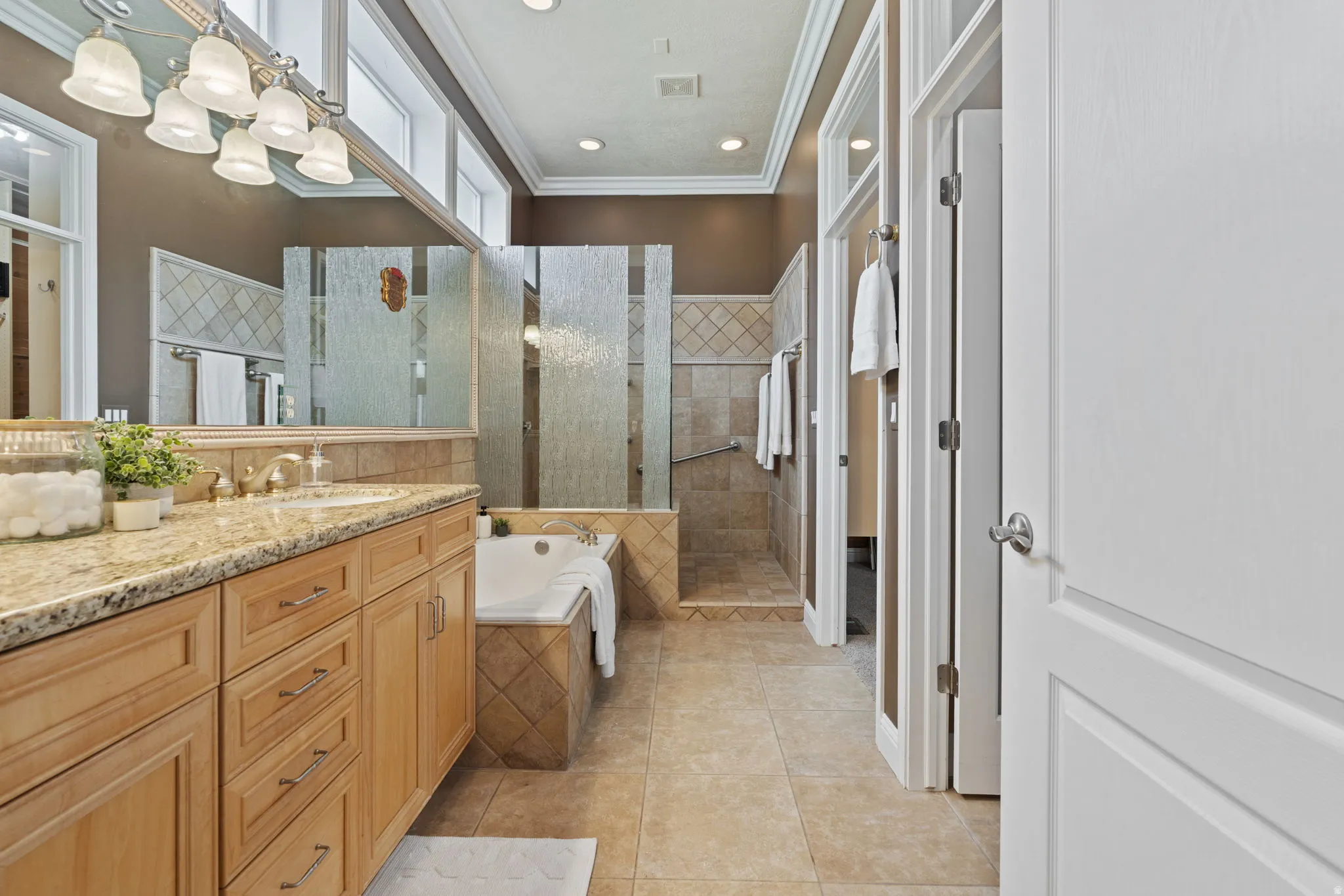 Full bathroom with walk in shower, a jetted tub, vanity, light tile patterned floors, and crown molding