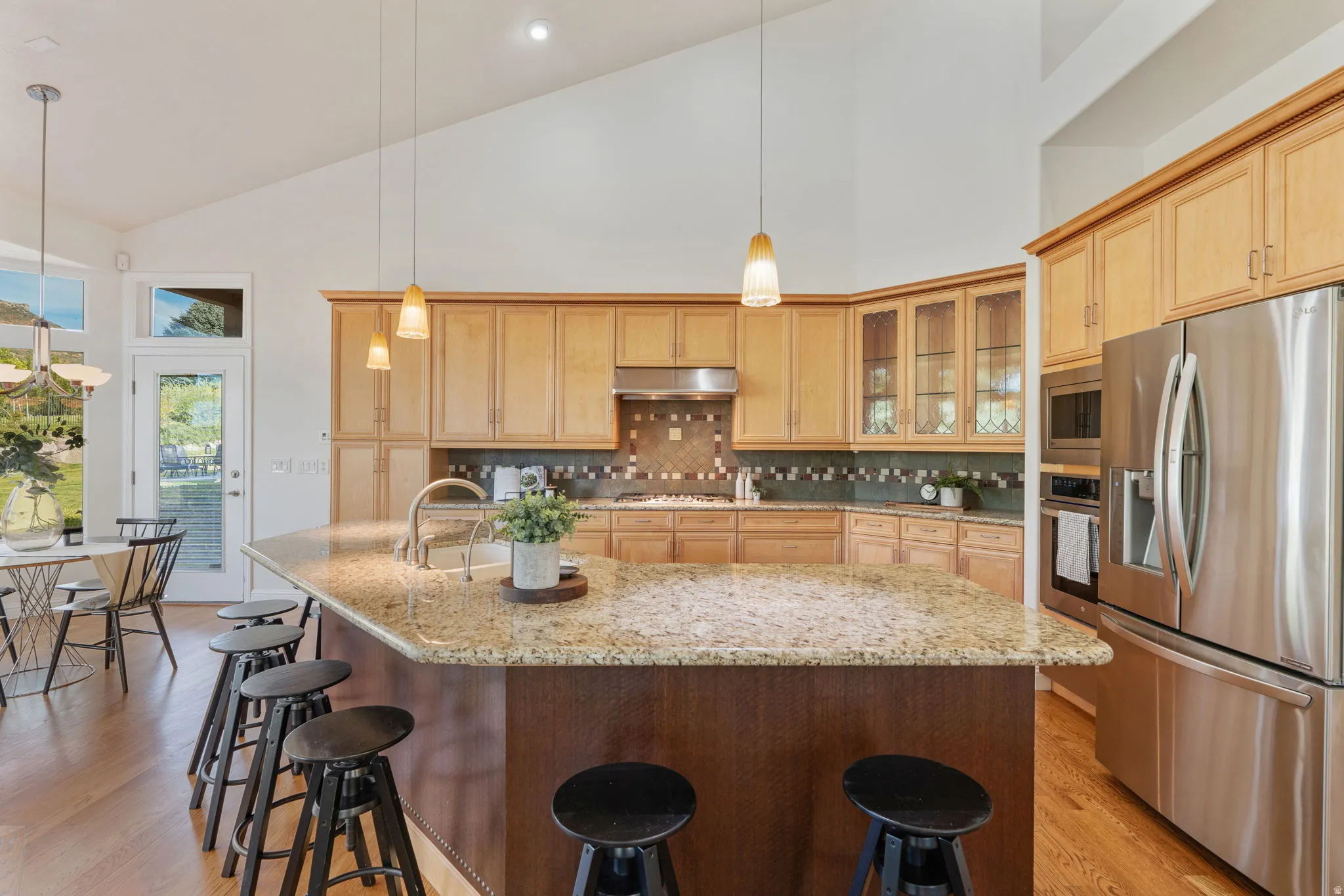 Kitchen with stainless steel appliances, glass insert cabinets, high vaulted ceiling, light stone counters, and decorative backsplash