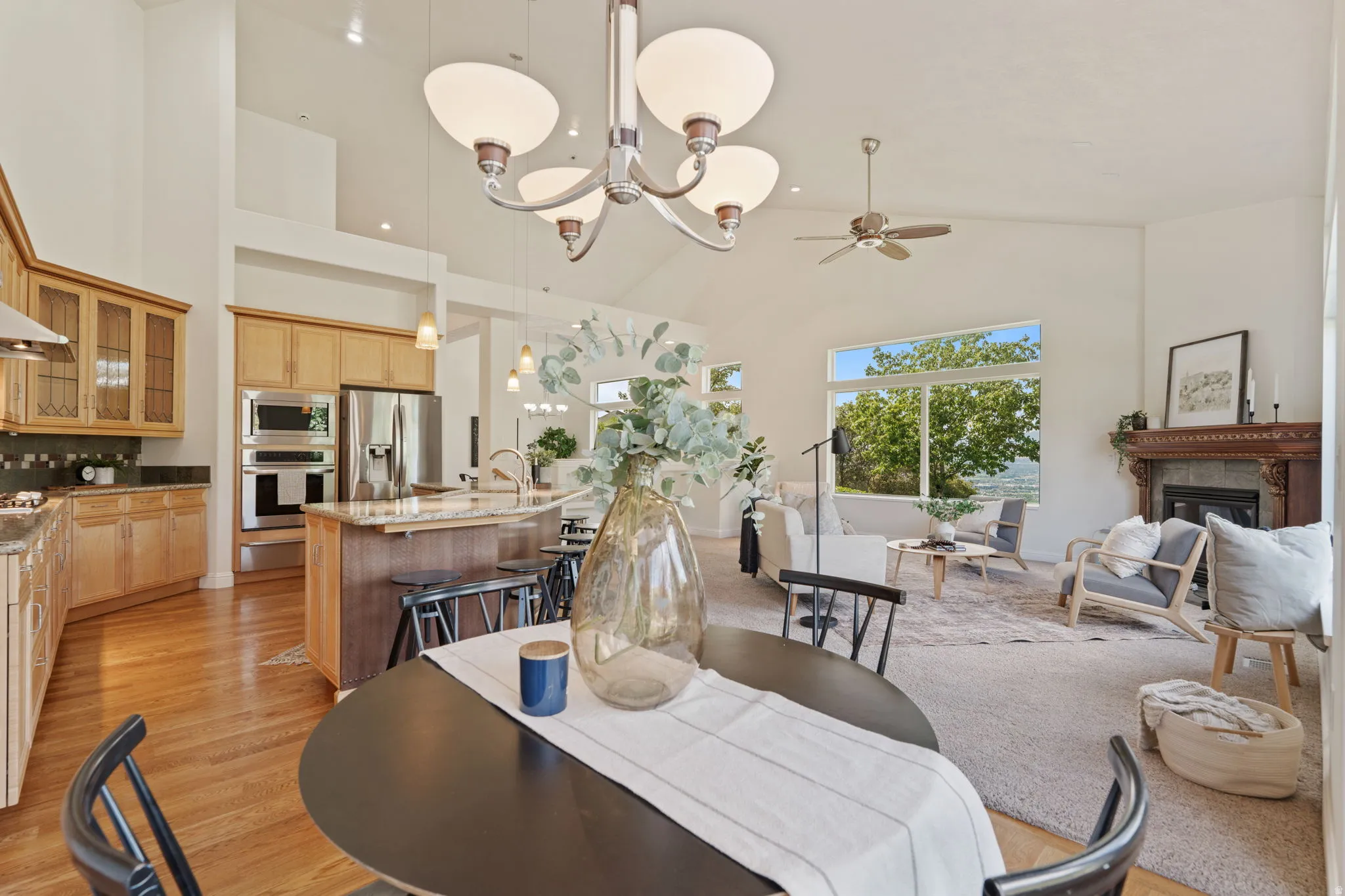 Dining room with a glass covered fireplace, a chandelier, a ceiling fan, high vaulted ceiling, and light wood-style floors
