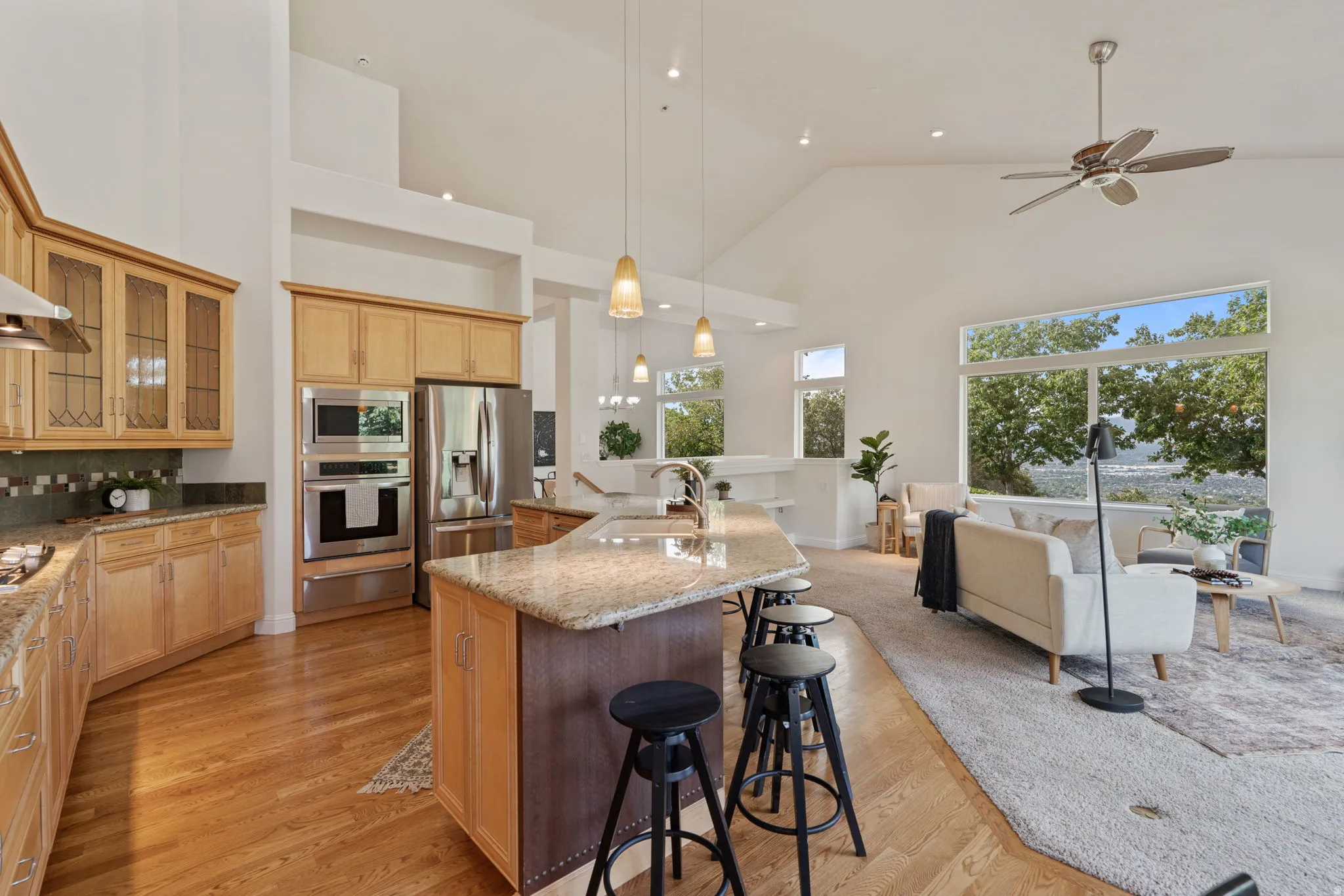 Kitchen featuring glass insert cabinets, a breakfast bar, hanging light fixtures, light stone countertops, and high vaulted ceiling