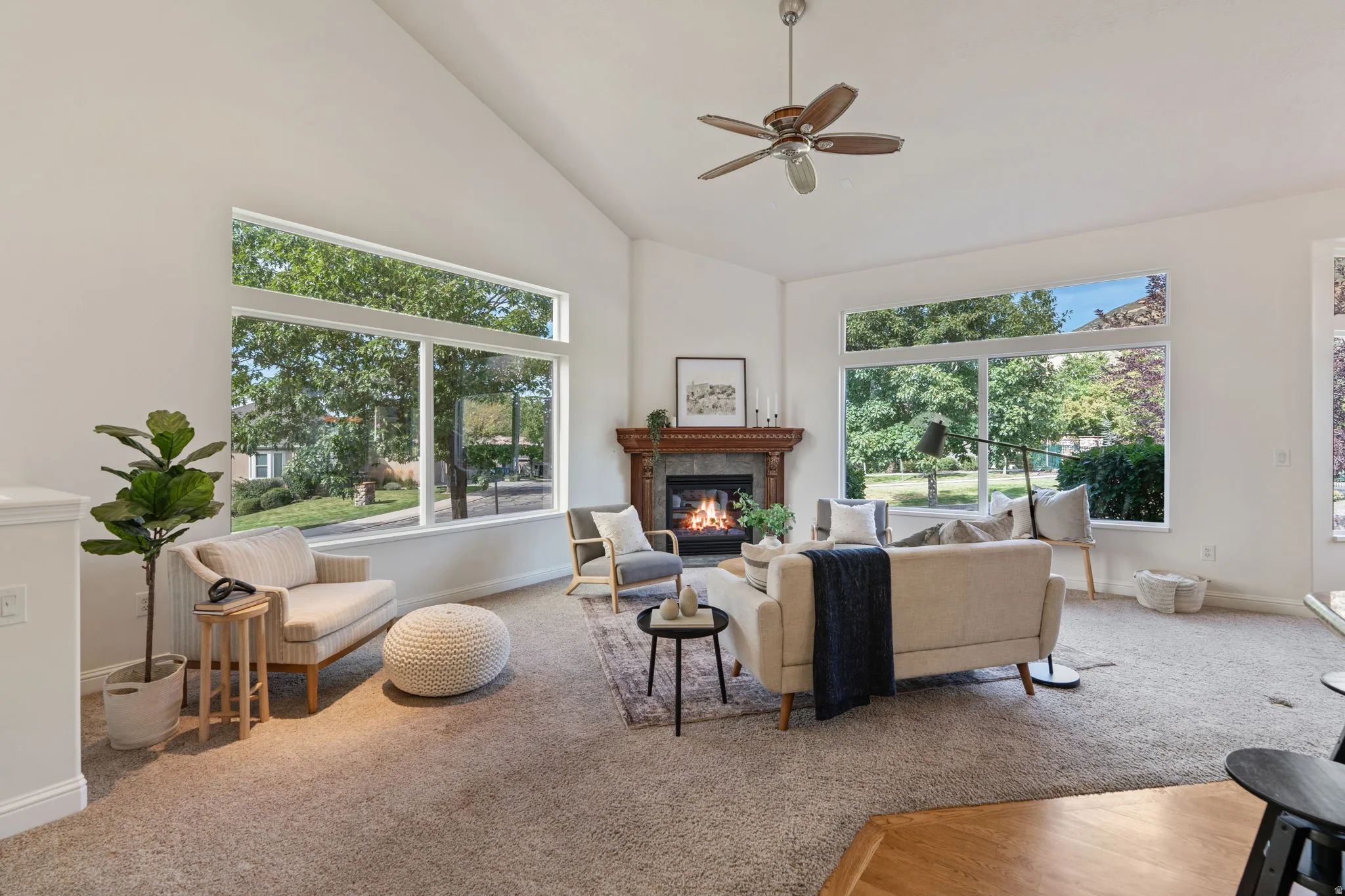 Carpeted living room with a glass covered fireplace, plenty of natural light, high vaulted ceiling, and ceiling fan