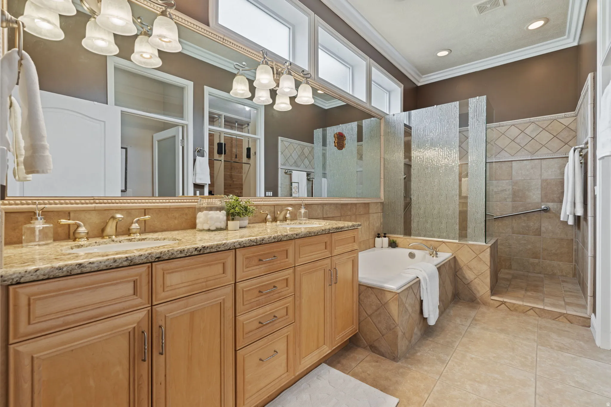Full bathroom featuring crown molding, double vanity, walk in shower, a jetted tub, and light tile patterned flooring