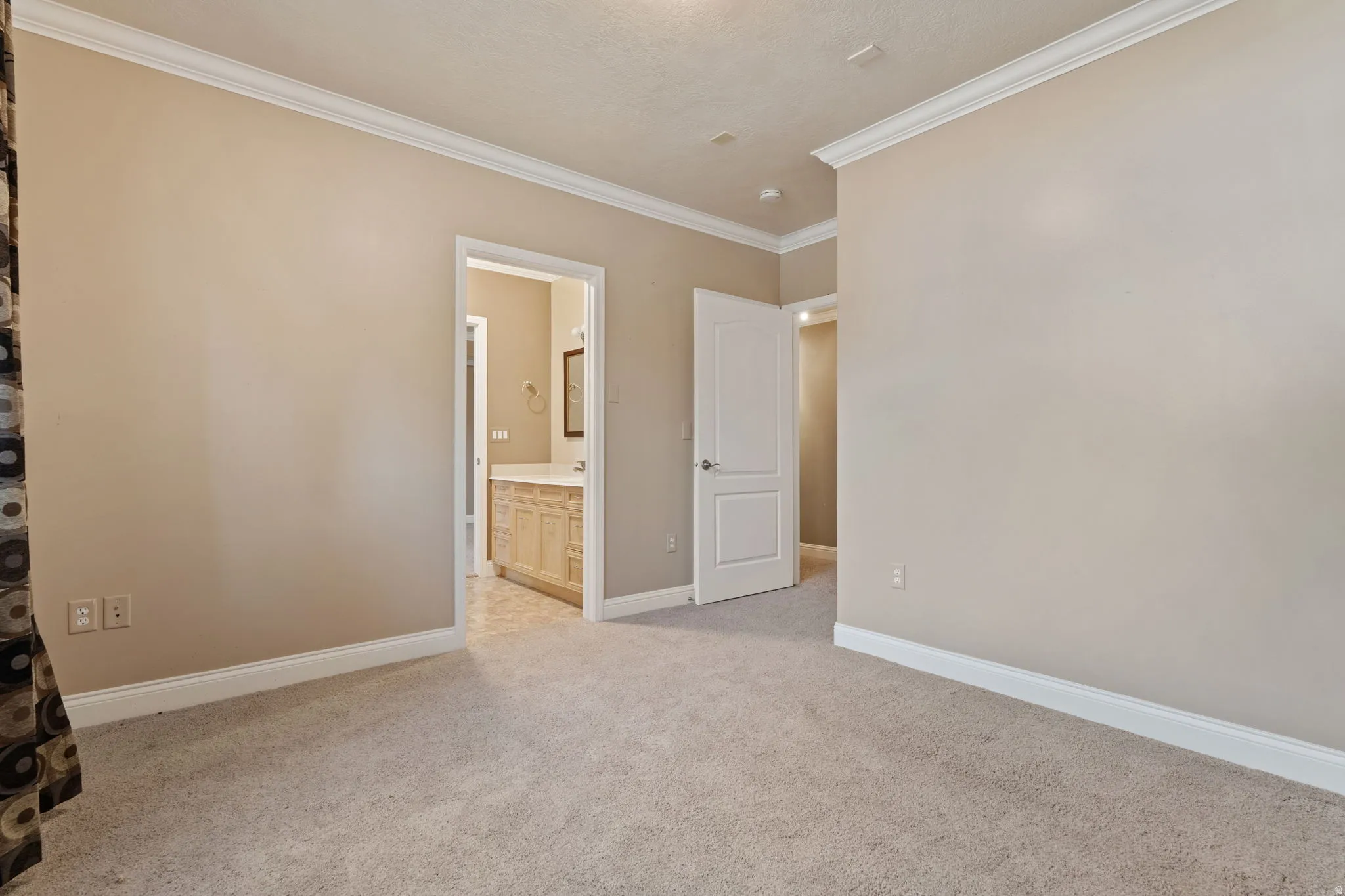Unfurnished bedroom featuring connected bathroom, crown molding, and light colored carpet