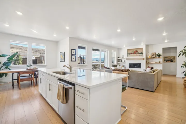 Kitchen with a kitchen island with sink, dishwasher, white cabinetry, a glass covered fireplace, and light wood-type flooring