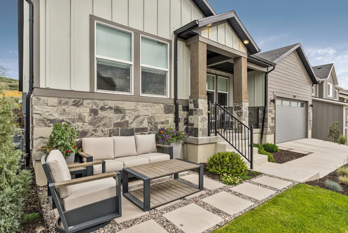 View of front of home featuring stone siding, an outdoor living space, board and batten siding, a garage, and driveway