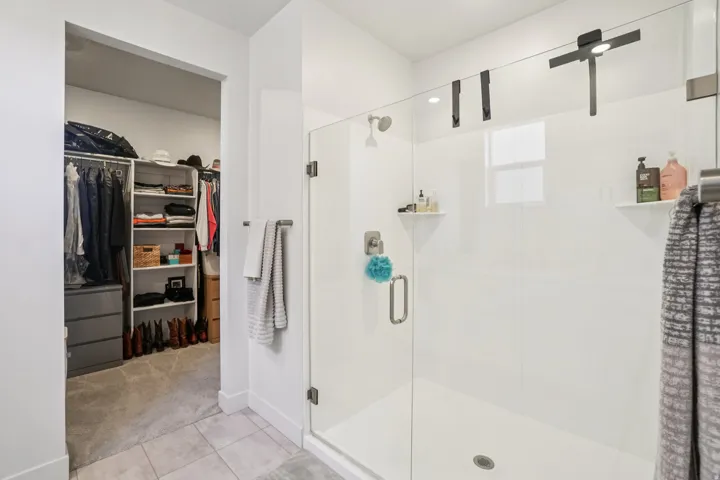Bathroom featuring a walk in closet, a stall shower, light tile patterned flooring, and light colored carpet