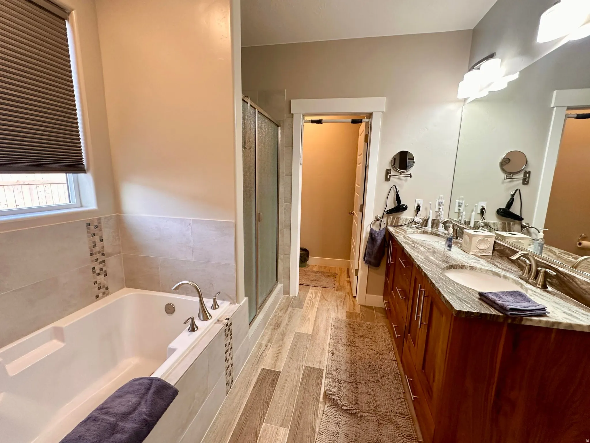 Bathroom with double vanity, wood tiled floors, a shower stall, and a bath