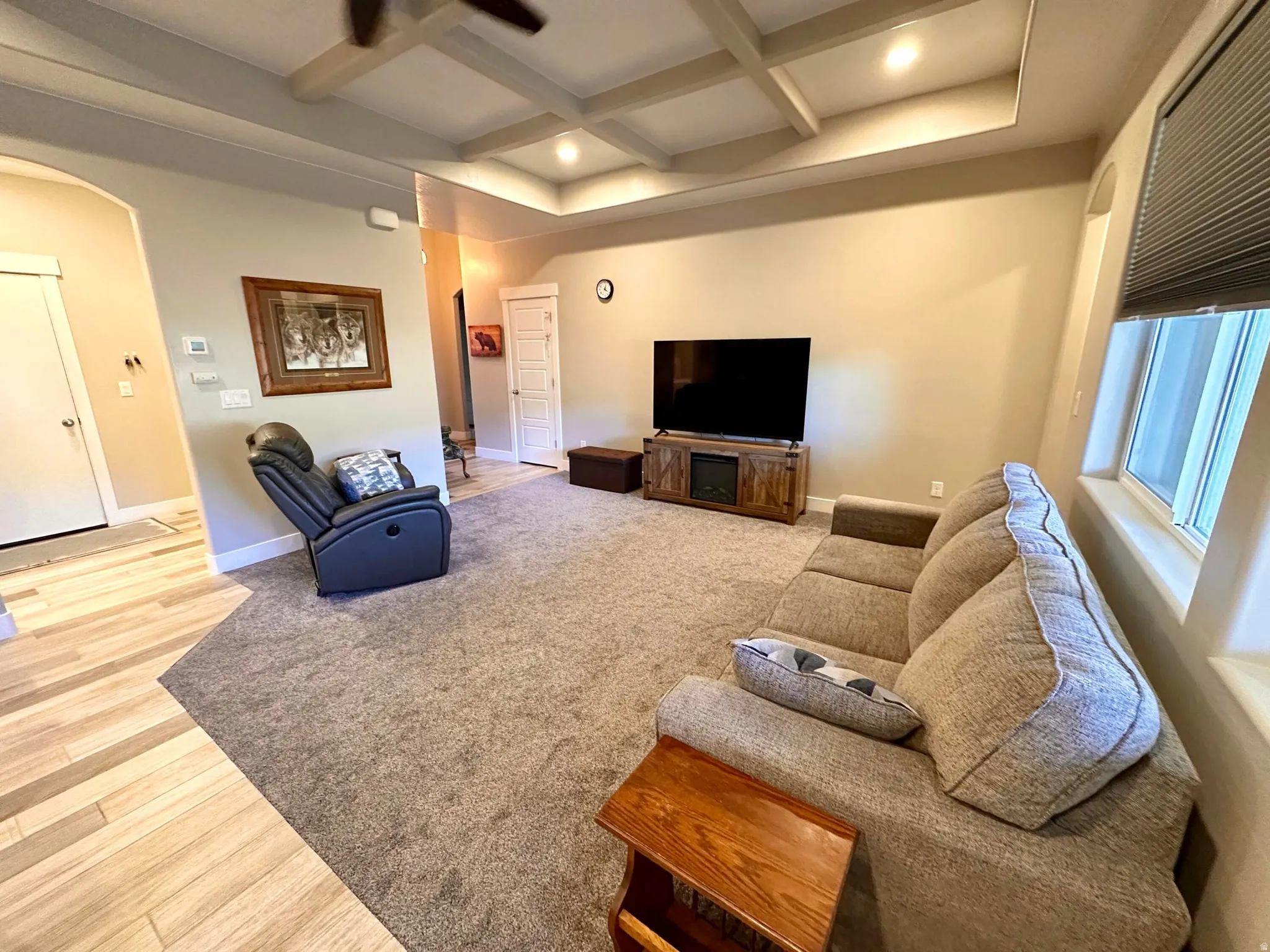Living room featuring arched walkways, coffered ceiling, beamed ceiling, recessed lighting, and light wood-style floors