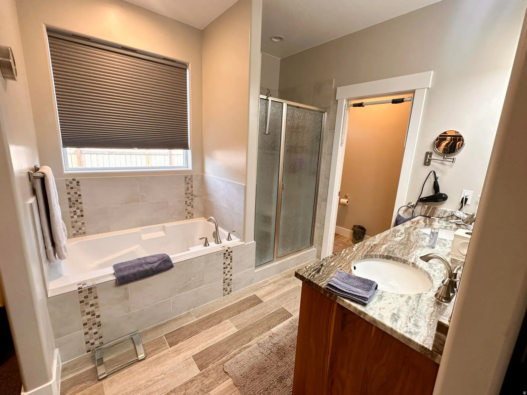 Full bath featuring a shower stall, double vanity, a bath, and wood tiled floors
