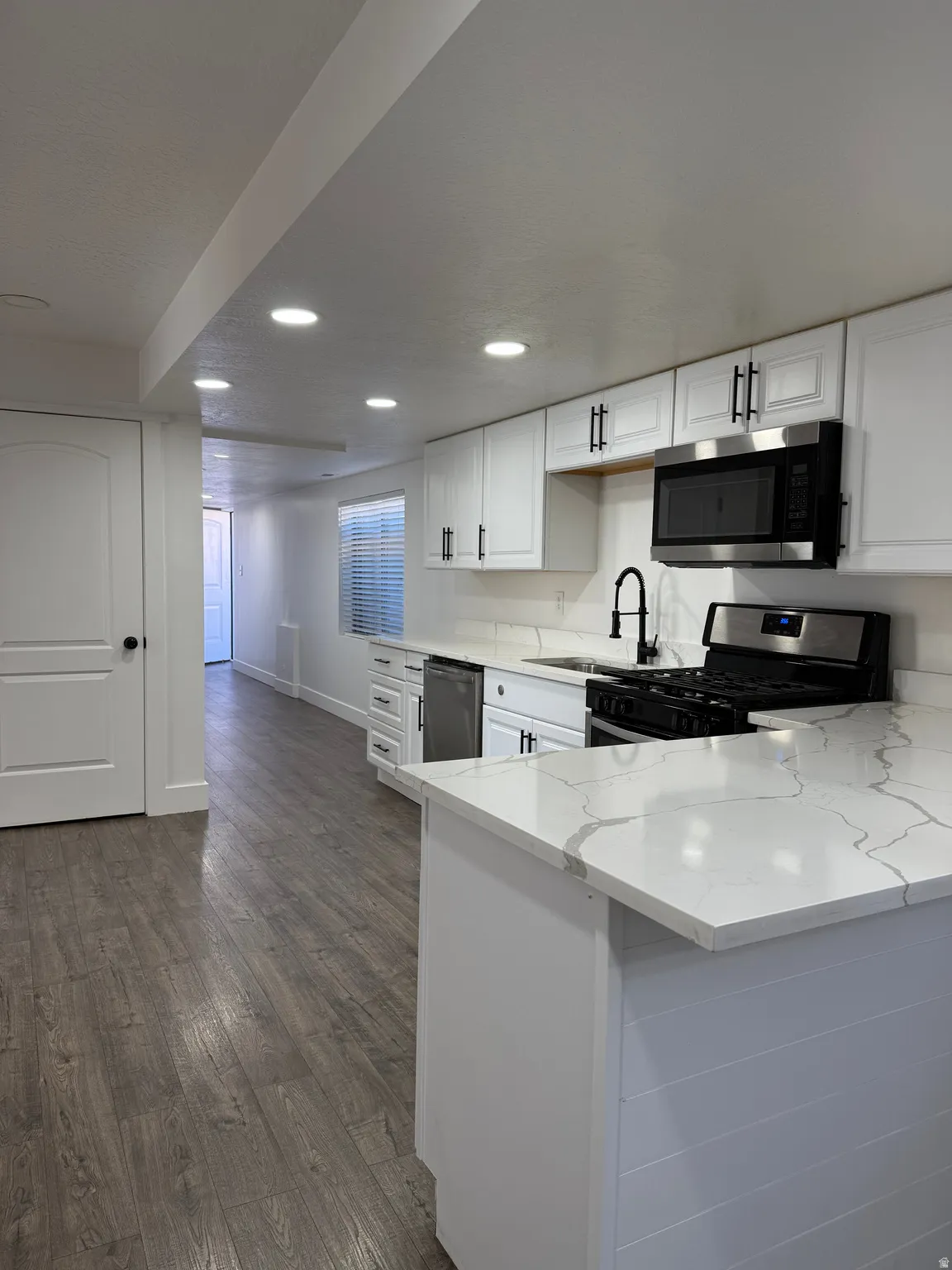 Kitchen featuring white cabinets, light stone countertops, appliances with stainless steel finishes, a peninsula, and dark wood-style floors
