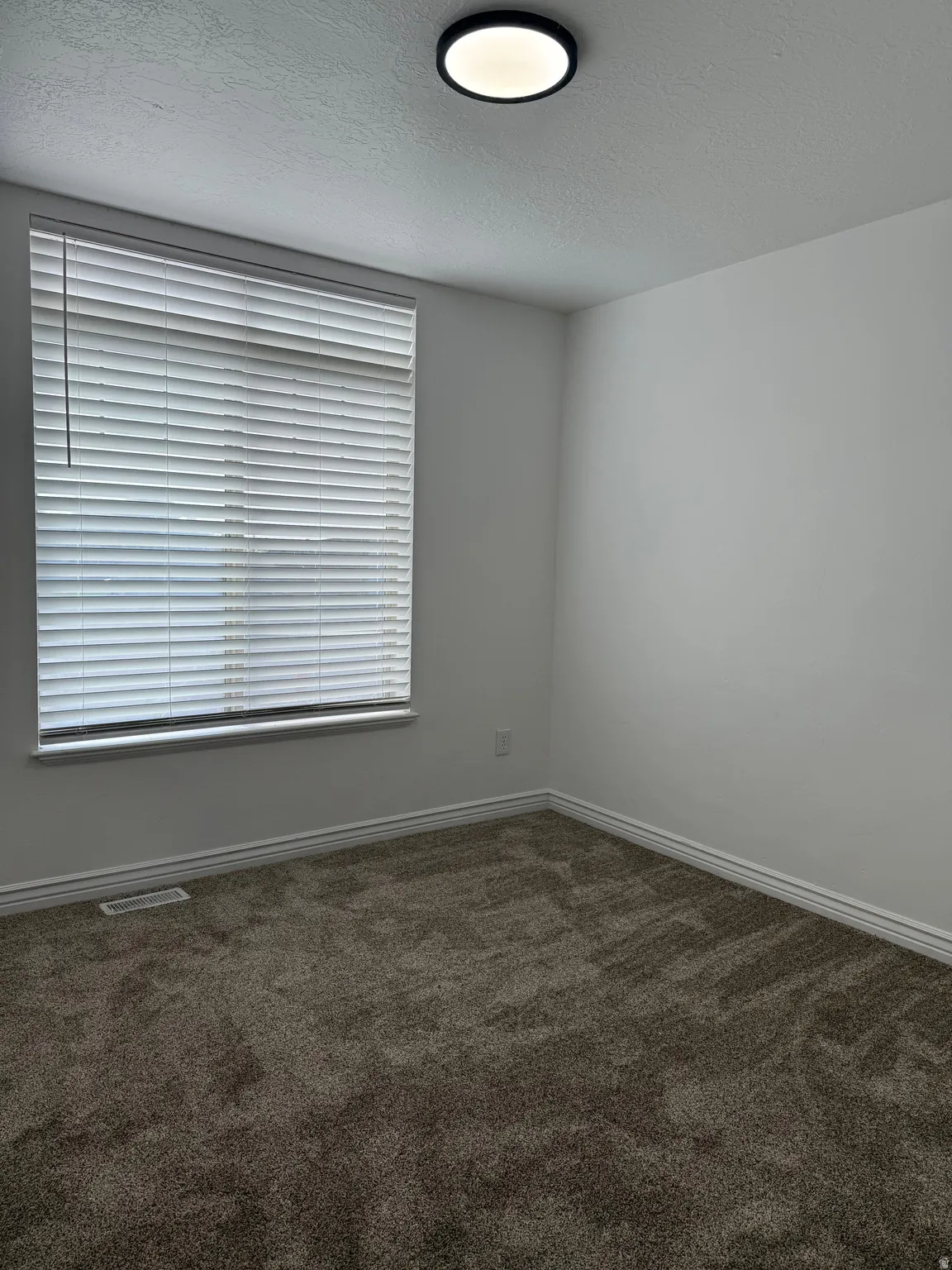 Empty room featuring a textured ceiling and dark colored carpet