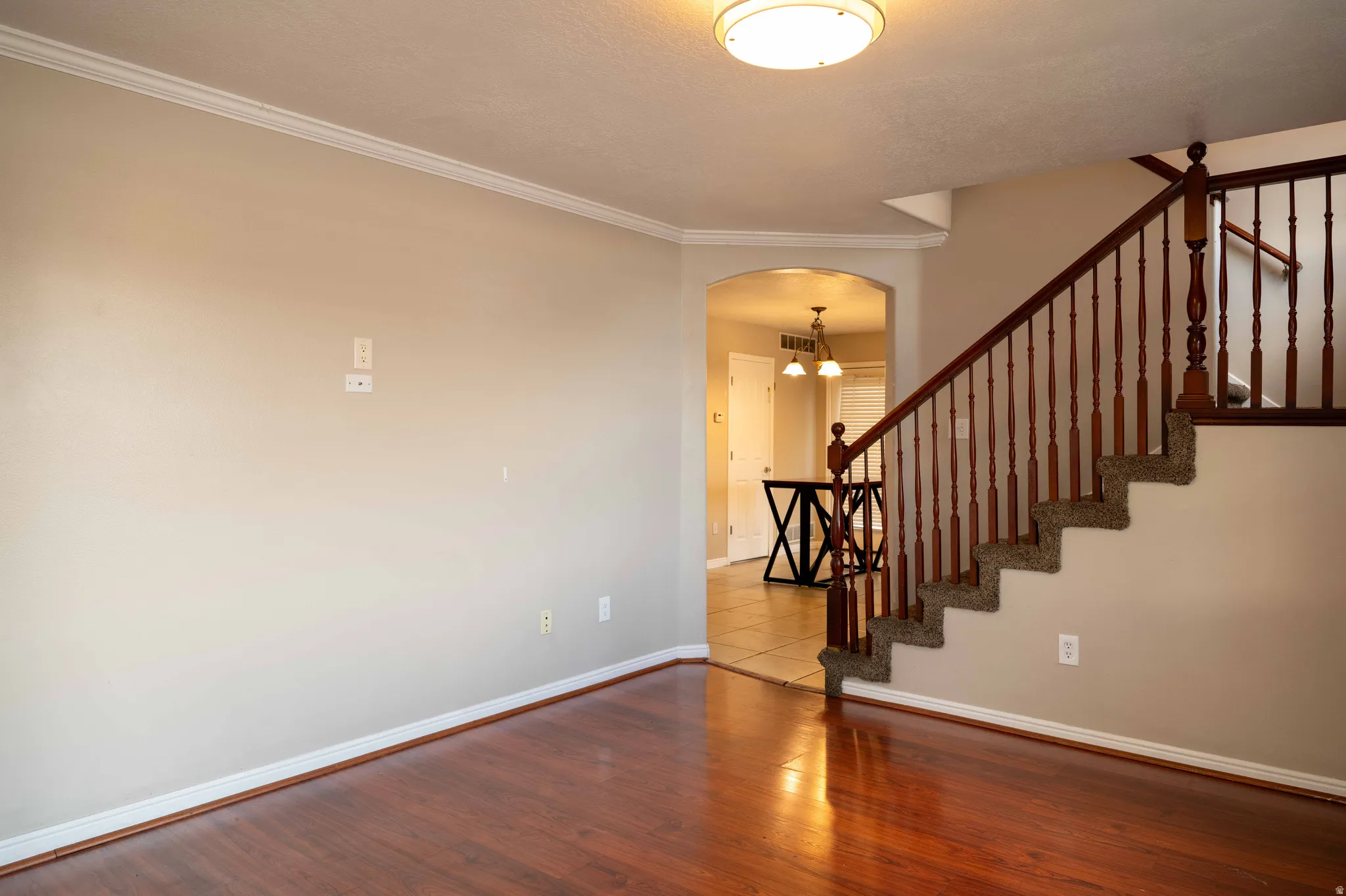 Stairway featuring crown molding, arched walkways, wood finished floors, and a chandelier