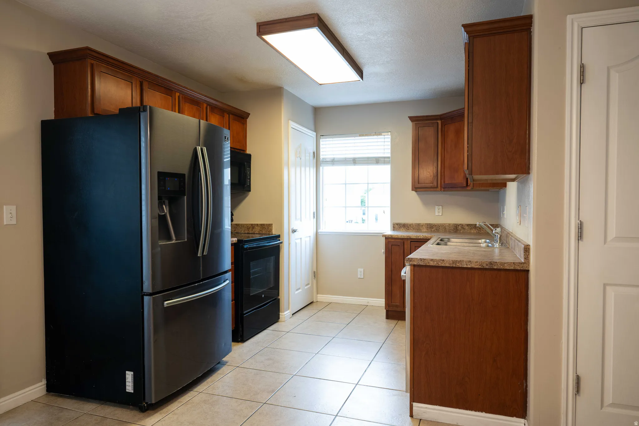 Kitchen featuring black appliances, brown cabinetry, and light tile patterned floors