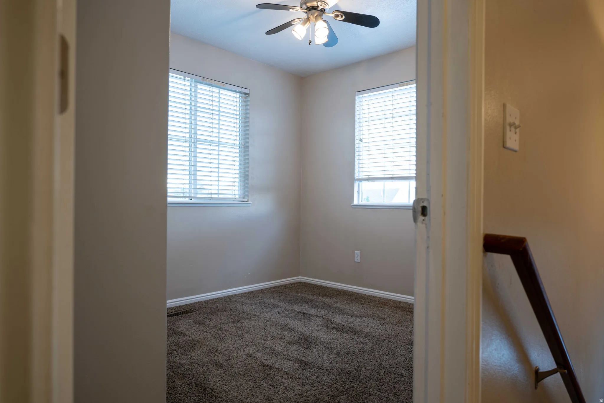 Empty room with dark colored carpet, plenty of natural light, and ceiling fan