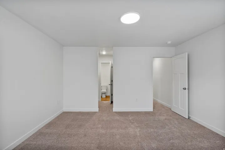 Unfurnished bedroom featuring light colored carpet and connected bathroom