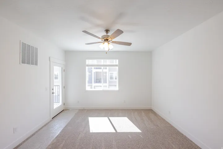 Bright room featuring light-toned carpet, a ceiling fan with integrated lighting, and white walls