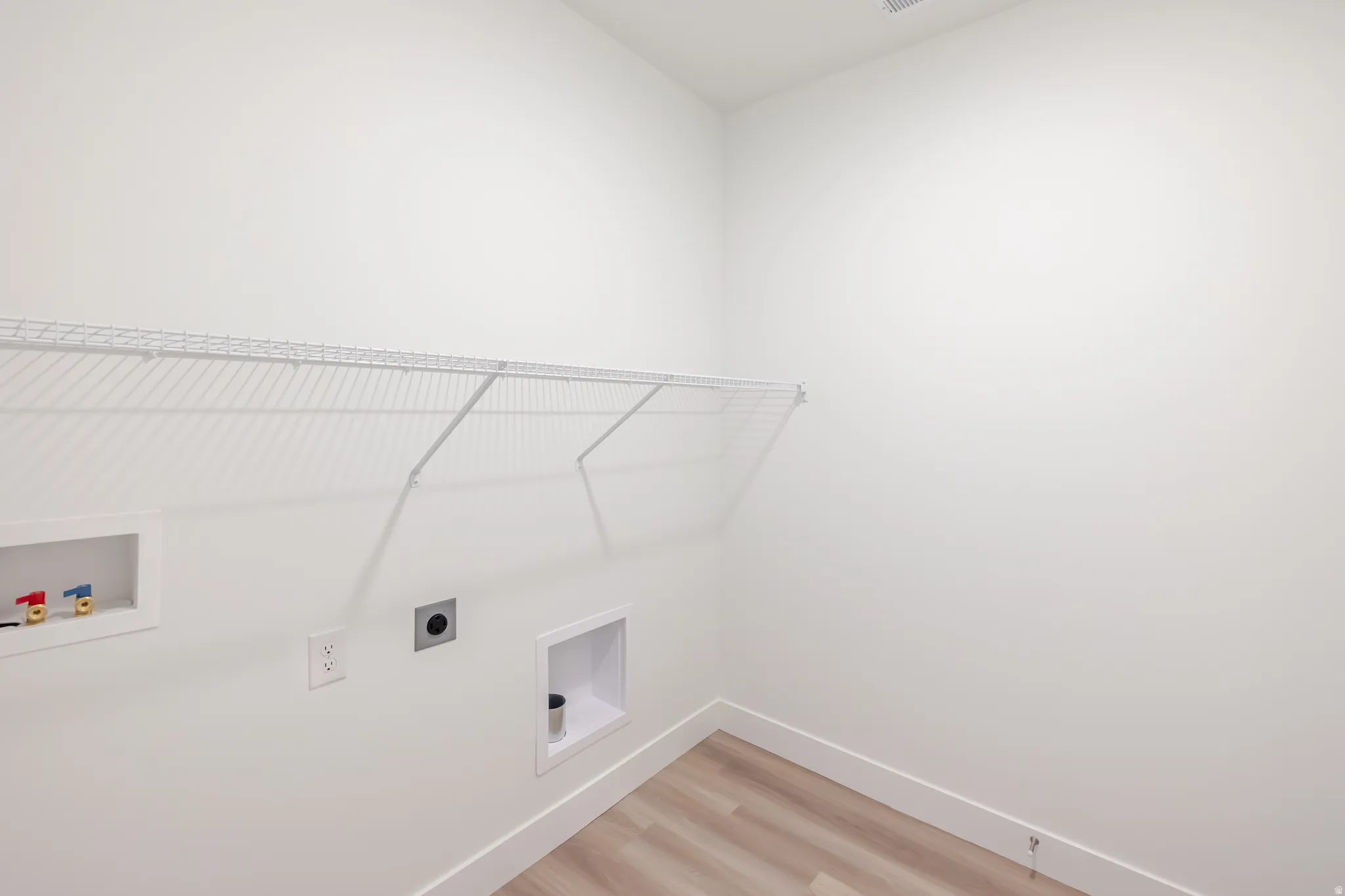 Laundry area with light wood-finish flooring and white baseboards