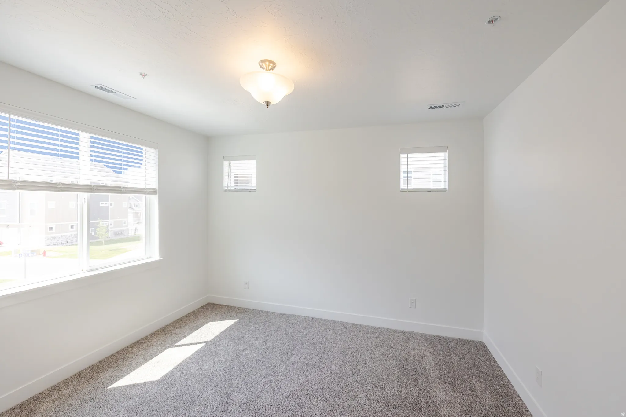 Carpeted room featuring multiple windows with blinds, white walls, and a ceiling-mounted light fixture