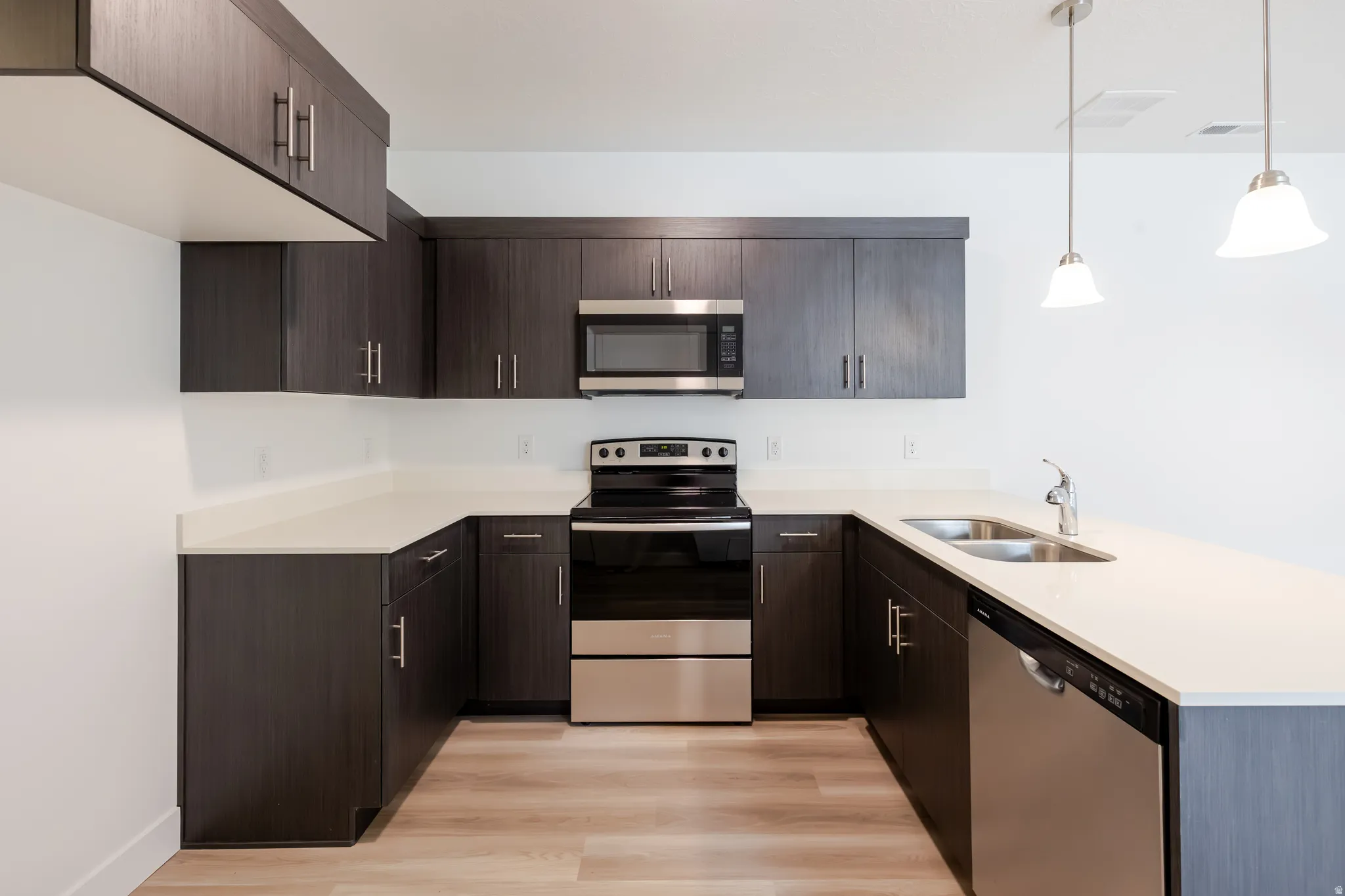 Modern kitchen featuring dark wood-finish cabinetry, stainless steel appliances, light-toned countertops, and wood-finish flooring
