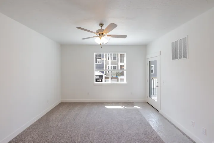 Spacious room featuring neutral carpet flooring, a ceiling fan with integrated lighting, and white walls