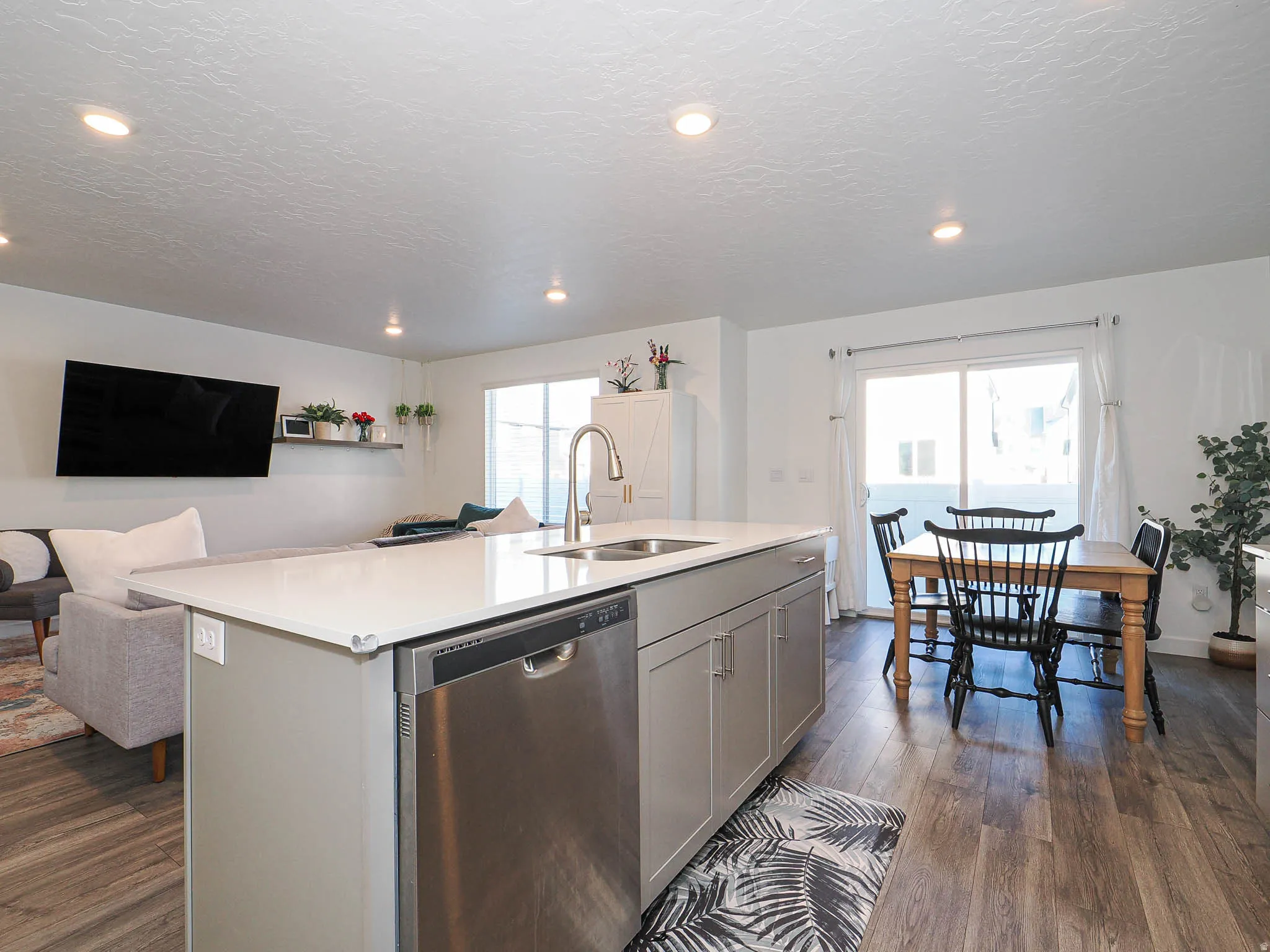 Kitchen featuring stainless steel dishwasher, a kitchen island with sink, gray cabinetry, dark wood-type flooring, and open floor plan
