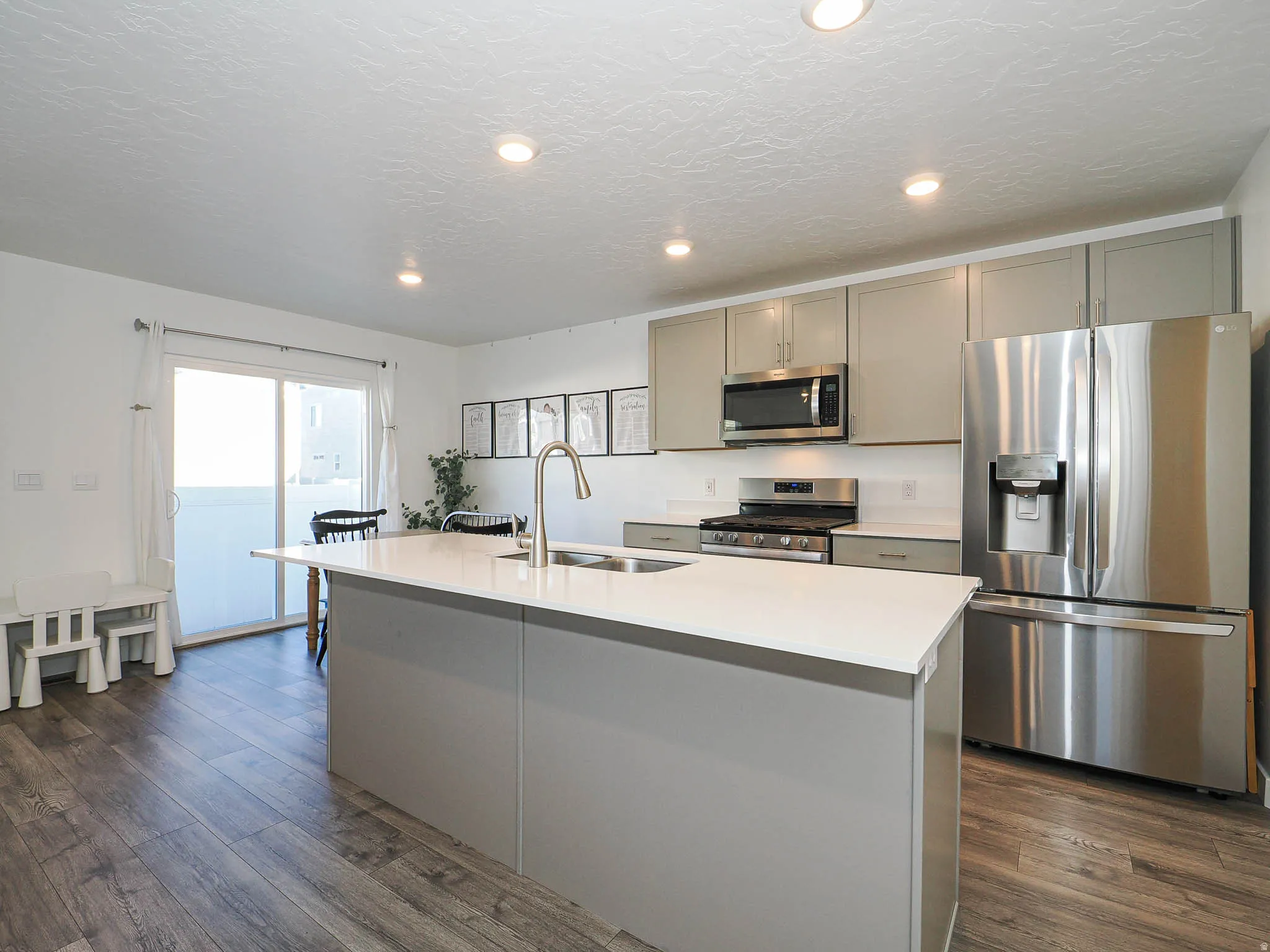 Kitchen with gray cabinets, appliances with stainless steel finishes, an island with sink, recessed lighting, and dark wood-type flooring