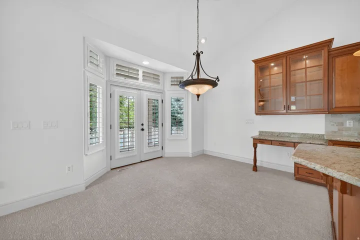 Bright dining area featuring French doors with transom windows and plantation shutters, a decorative chandelier, and built-in cabinetry with glass fronts