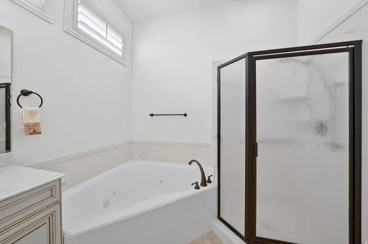 Bathroom featuring a white jetted soaking tub with bronze fixtures, a framed glass shower enclosure, and a vanity with a white countertop and integrated sink