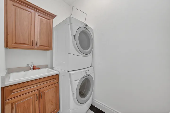 Laundry area featuring a stacked washer and dryer, wood cabinetry, a utility sink, and light-toned countertops