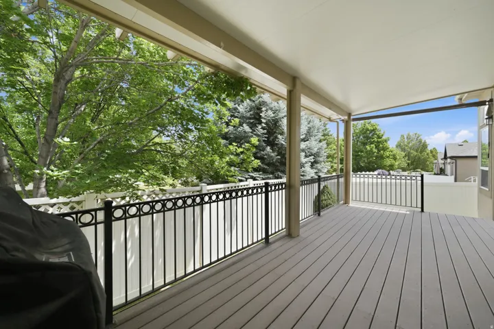 Spacious covered deck featuring composite decking, black metal railings with circular accents, and white privacy fencing