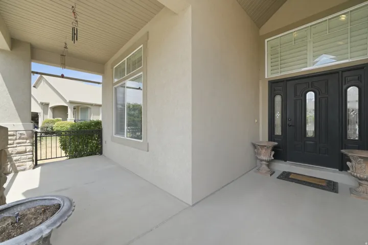 Entryway featuring a double door with decorative glass inserts, a transom window with plantation shutters, and a covered porch with a stone column base