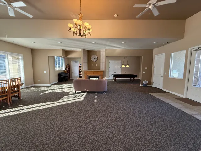 Clubhouse living area featuring a ceiling fan, a fireplace, carpet floors, and a chandelier