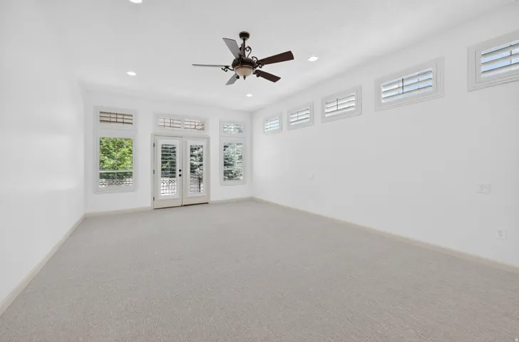 Spacious room featuring light-toned carpet flooring, a ceiling fan, recessed lighting, and multiple windows with white plantation shutters
