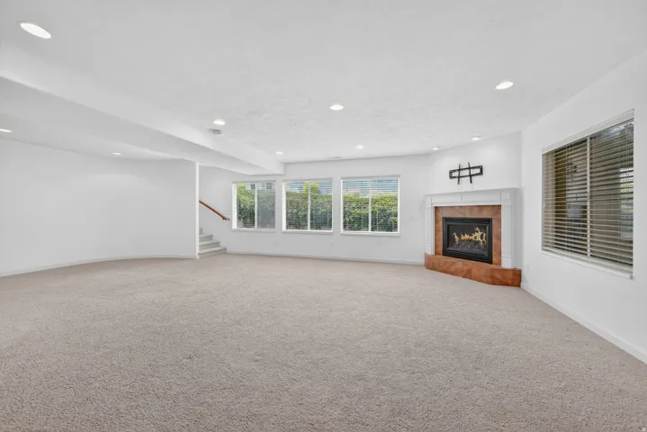 Spacious room featuring neutral carpeting and a corner fireplace with a white mantel and stone surround