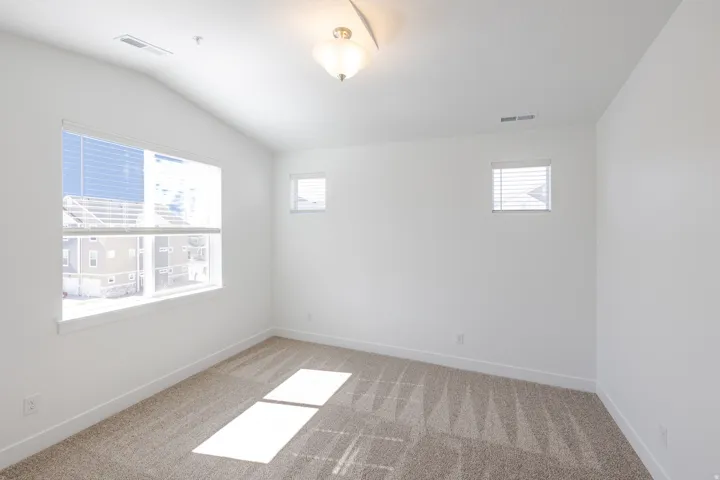 Bright interior room featuring a large window, two smaller windows, vaulted ceilings, and neutral-toned carpet flooring