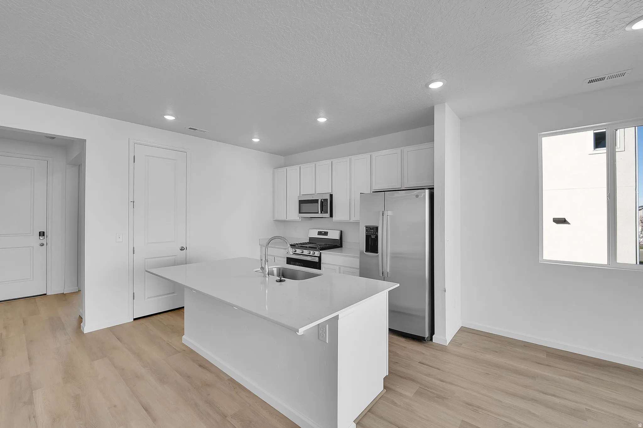 Kitchen with appliances with stainless steel finishes, a center island with sink, white cabinetry, recessed lighting, and light wood-type flooring