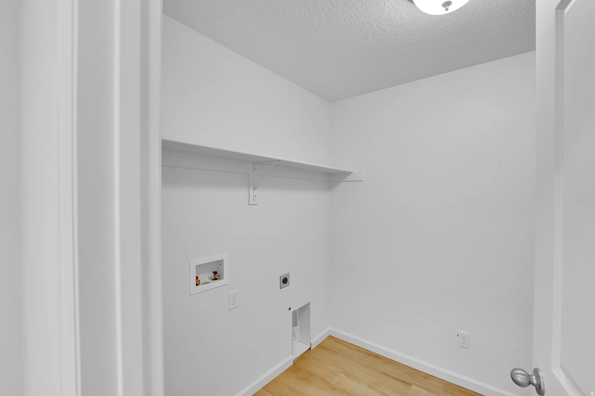 Laundry room featuring light wood-type flooring, washer hookup, hookup for an electric dryer, and a textured ceiling