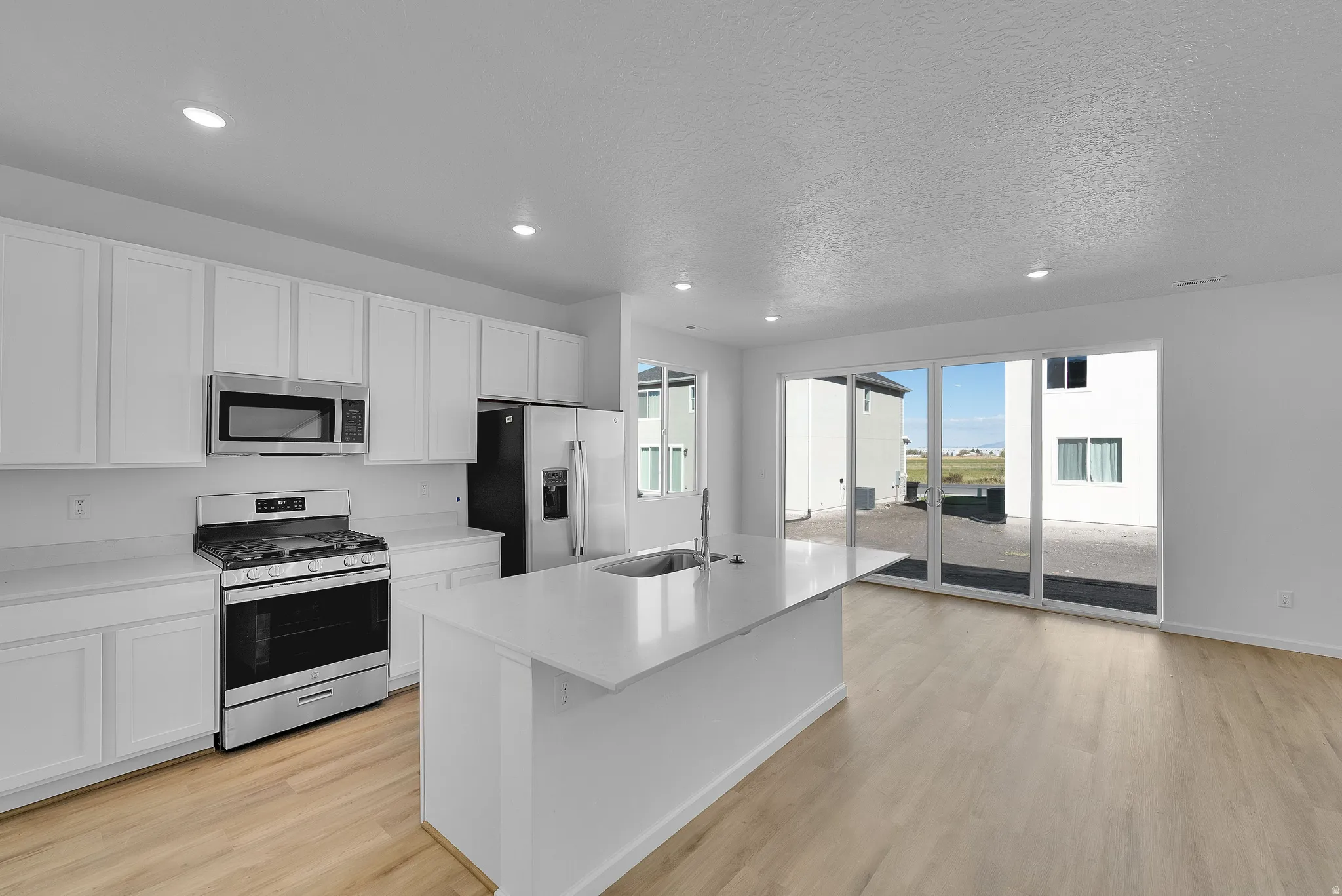 Kitchen with stainless steel appliances, white cabinets, a center island with sink, recessed lighting, and light wood-style flooring