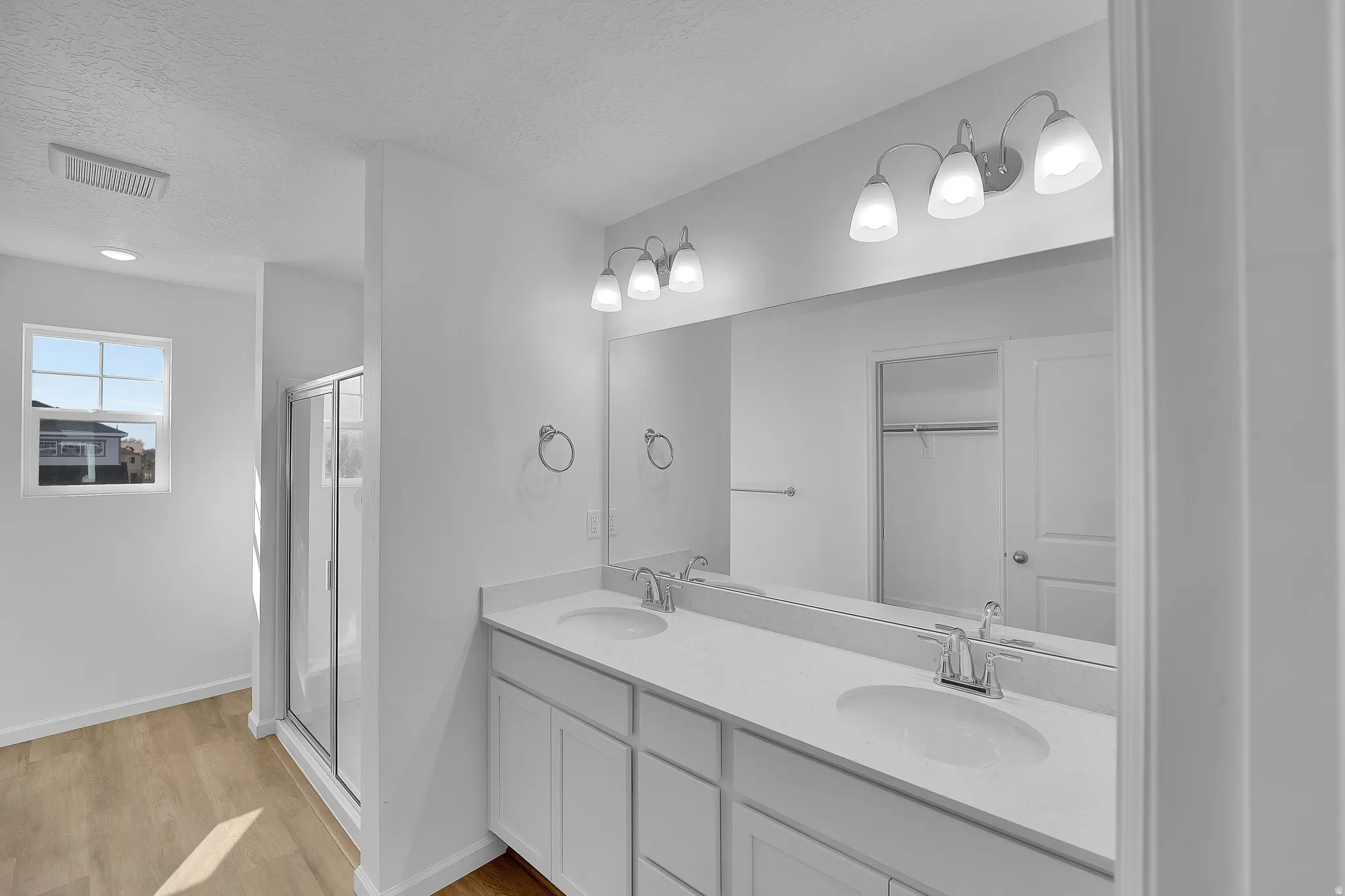 Full bathroom featuring double vanity, a stall shower, light wood-style floors, a textured ceiling, and a spacious closet
