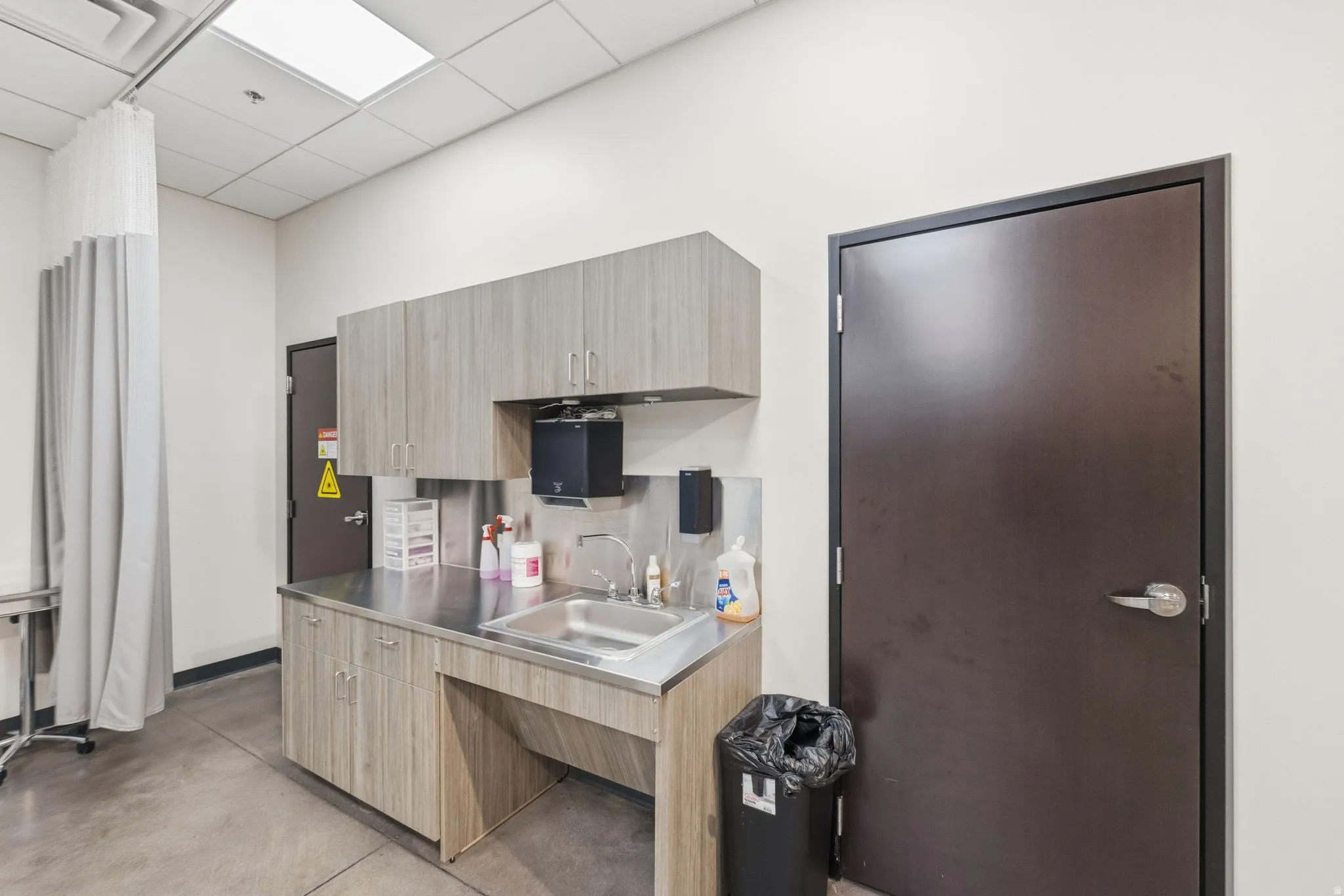 Kitchen featuring finished concrete floors, stainless steel countertops, decorative backsplash, light brown cabinets, and a paneled ceiling