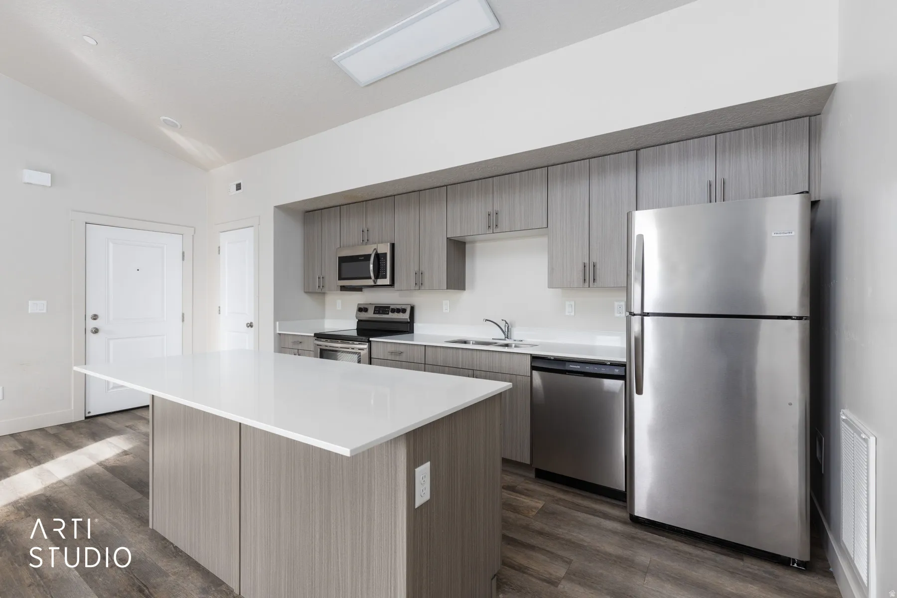 Kitchen with stainless steel appliances, vaulted ceiling, a kitchen island, dark wood-type flooring, and light stone countertops