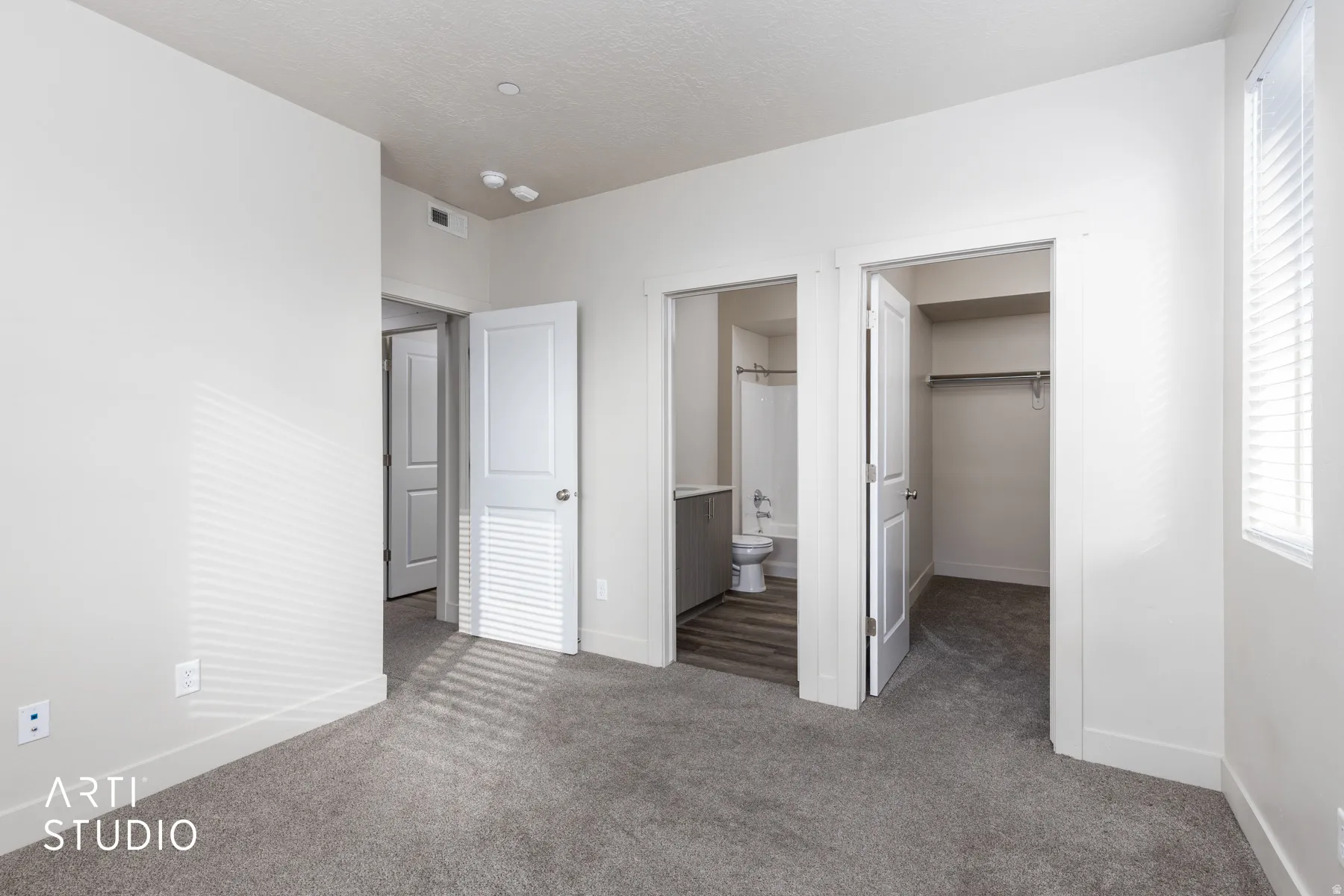 Unfurnished bedroom featuring dark carpet, a walk in closet, and ensuite bathroom