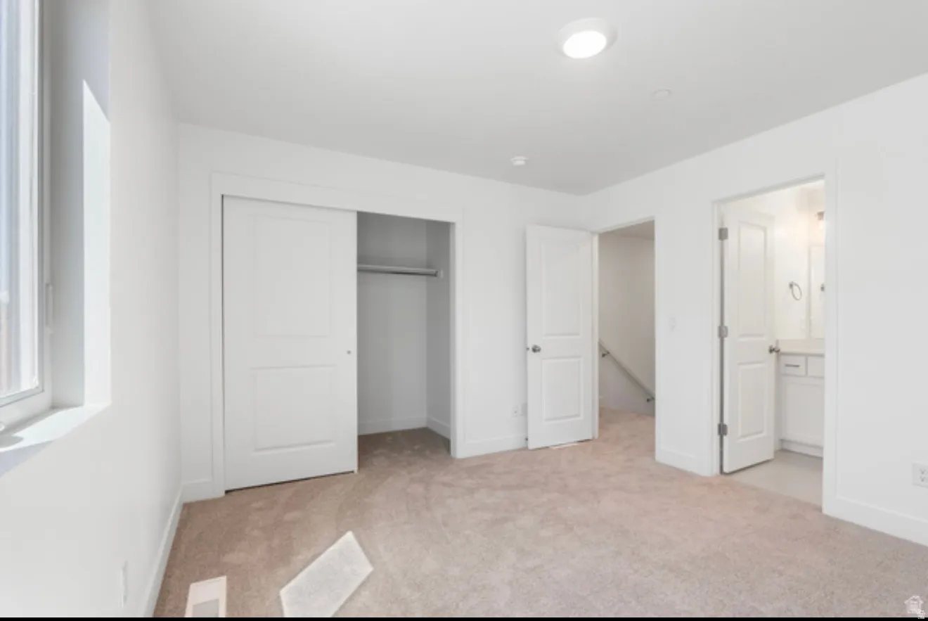 Unfurnished bedroom featuring light colored carpet, a closet, and ensuite bathroom