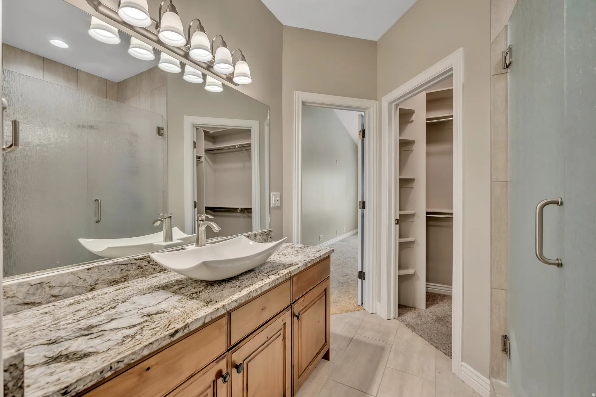 Bathroom featuring a walk in closet, vanity, a stall shower, light colored carpet, and light tile patterned flooring