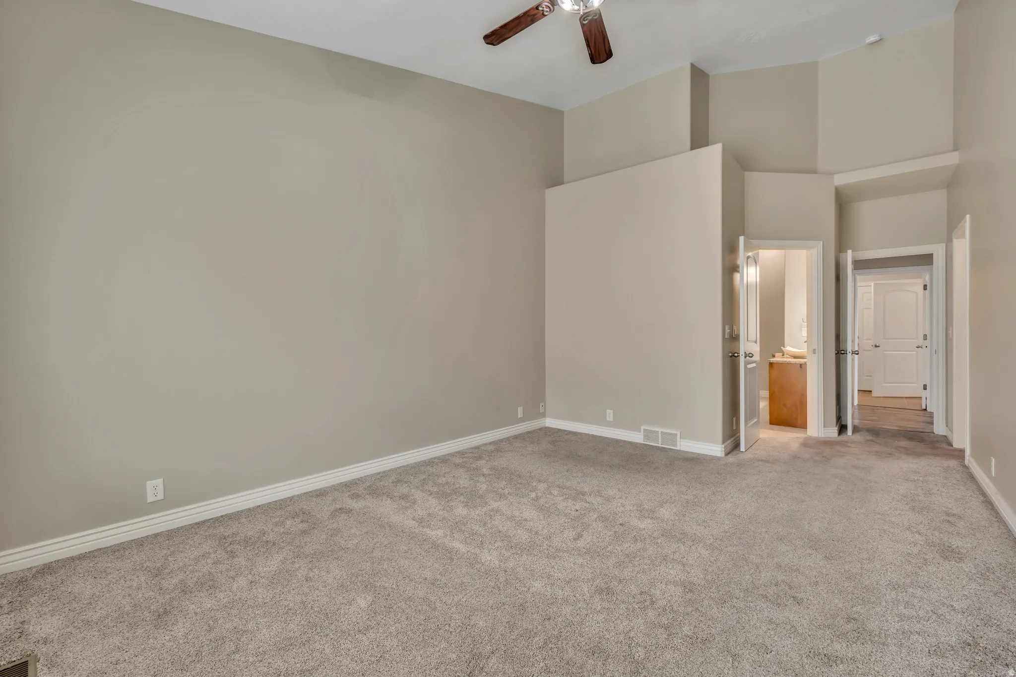 Unfurnished bedroom featuring ensuite bath, light colored carpet, ceiling fan, and a high ceiling