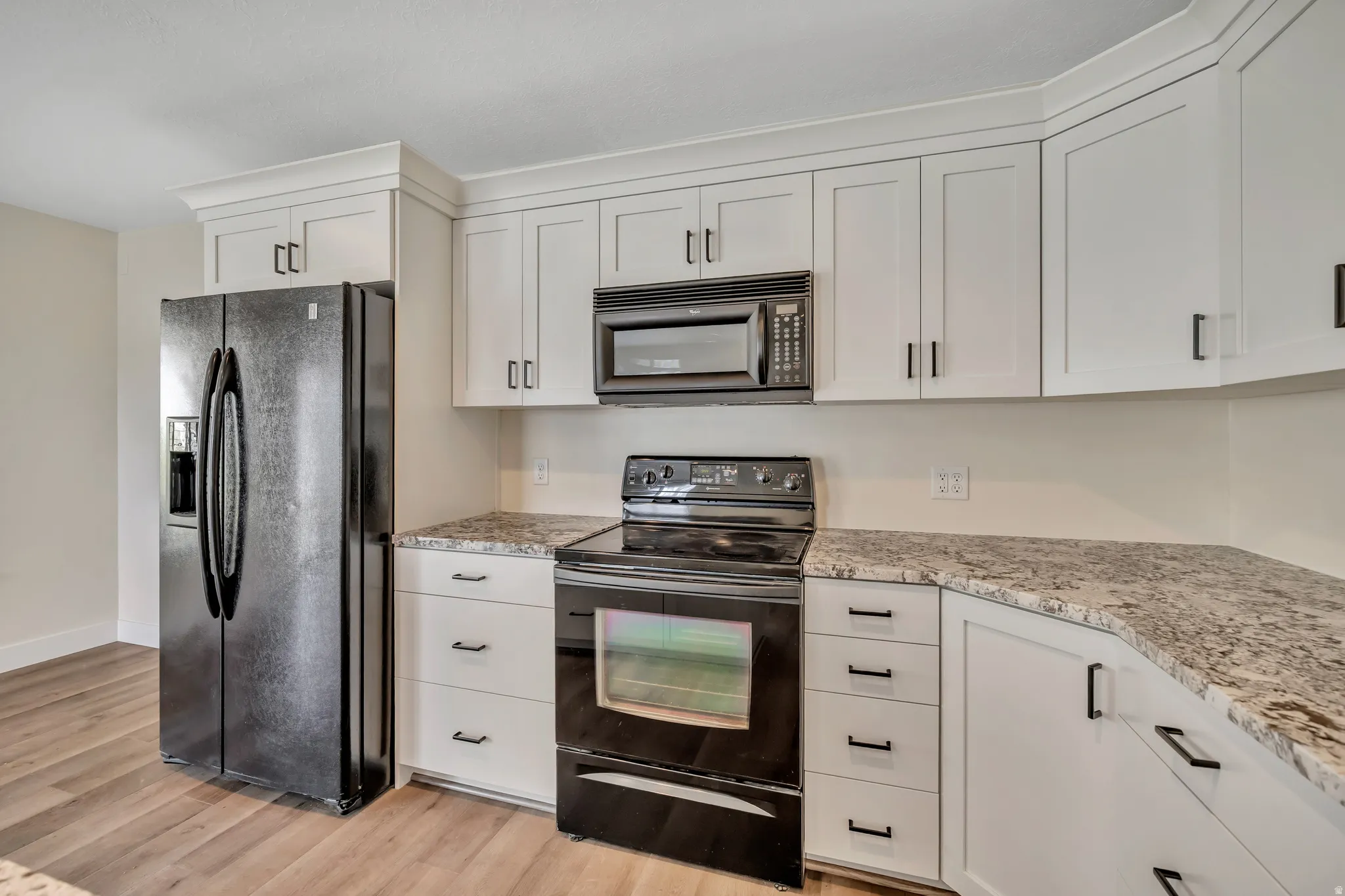 Kitchen with black appliances, white cabinetry, light wood-type flooring, and light stone counters