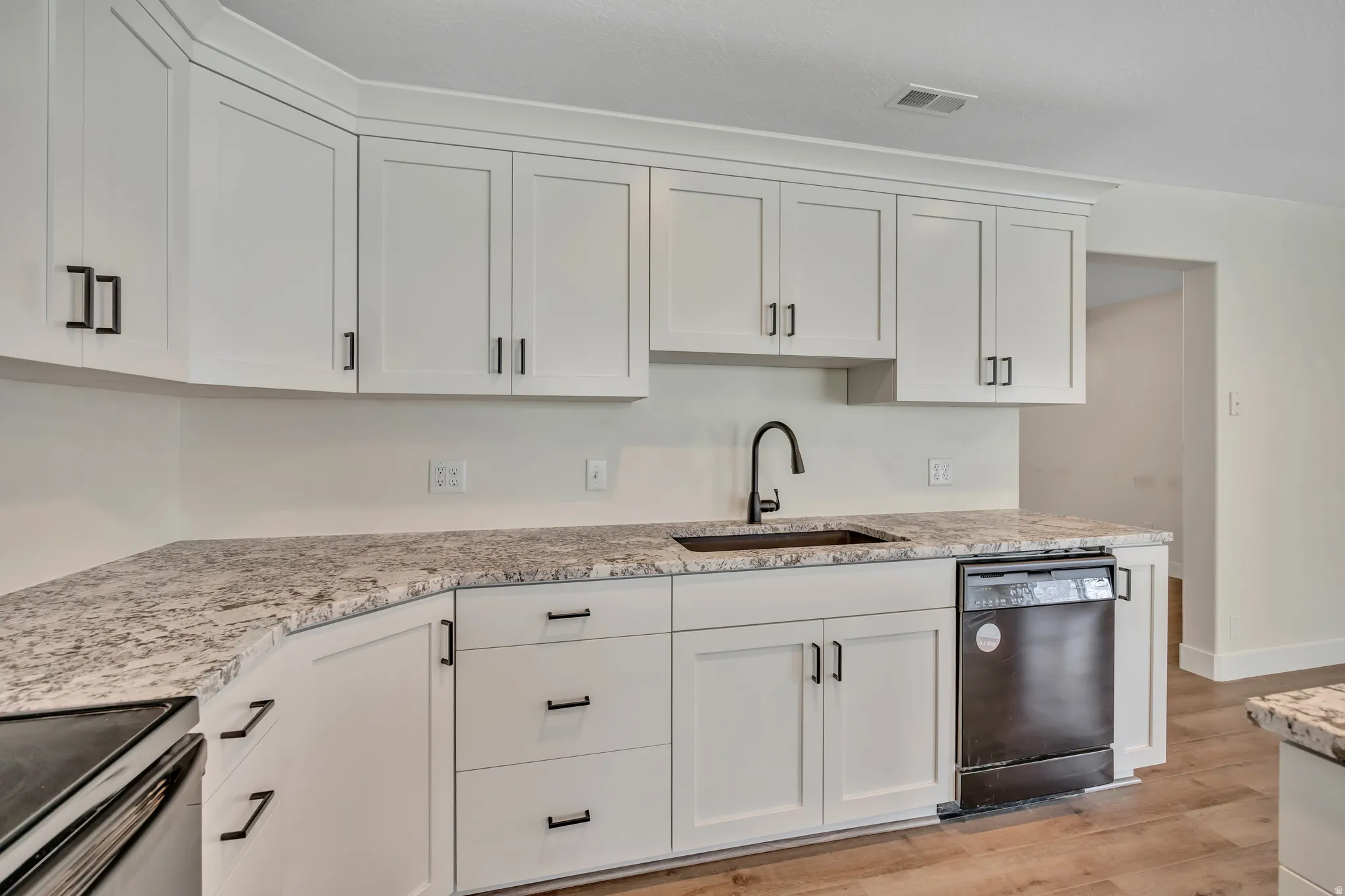 Kitchen with white cabinets, black appliances, light stone countertops, and light wood-type flooring